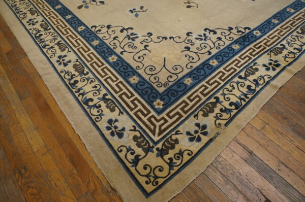 The corner of a cream and blue rug with geometric and floral patterns sits on rustic wood flooring.