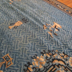 Faded blue rug with geometric fretwork and stylized tan motifs visible on wood plank flooring.