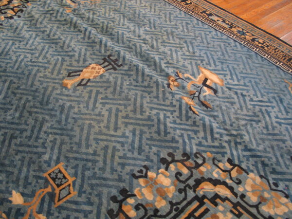 Faded blue rug with geometric fretwork and stylized tan motifs visible on wood plank flooring.