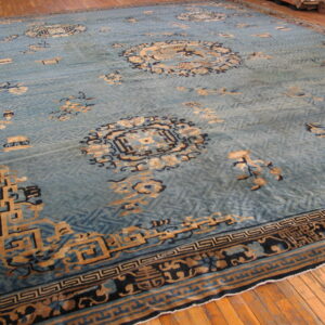 Light blue rug with tan and navy detailed motifs over a subtle geometric field on wood floor.