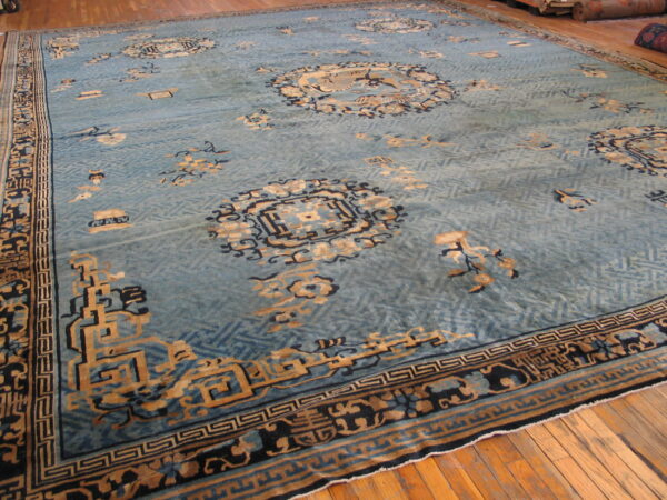 Light blue rug with tan and navy detailed motifs over a subtle geometric field on wood floor.