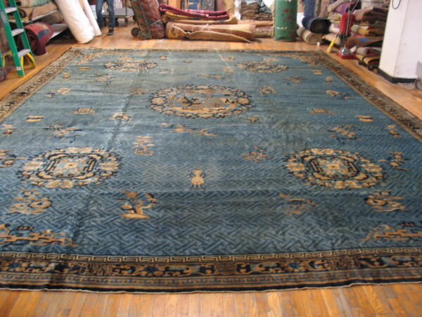 Large, low-pile rug with a blue lattice field and tan medallions on hardwood plank flooring.