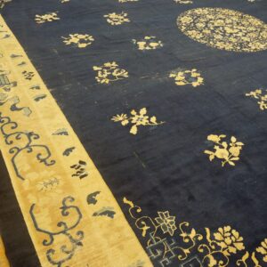 Dark navy blue area rug with gold and light blue floral designs and a wide striped border on wood flooring.