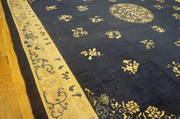 Dark navy blue area rug with gold and light blue floral designs and a wide striped border on wood flooring.