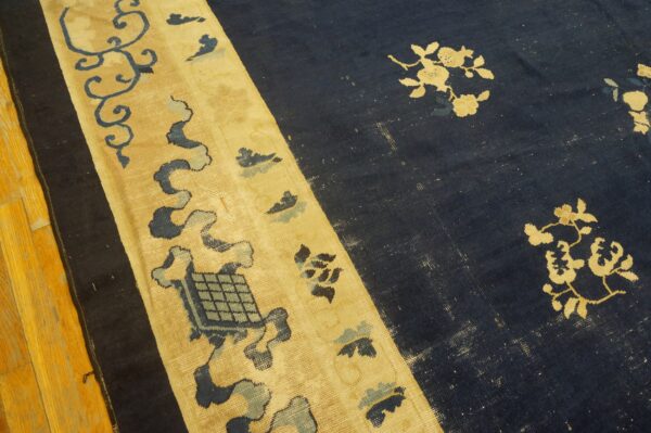 Distressed navy blue rug with gold floral motifs and a wide patterned tan border on hardwood flooring.