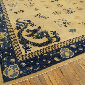 Cream and blue rug featuring a dragon and geometric border motifs lying on yellow-toned wood flooring.