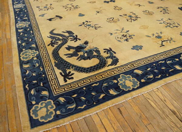 Cream and blue rug featuring a dragon and geometric border motifs lying on yellow-toned wood flooring.