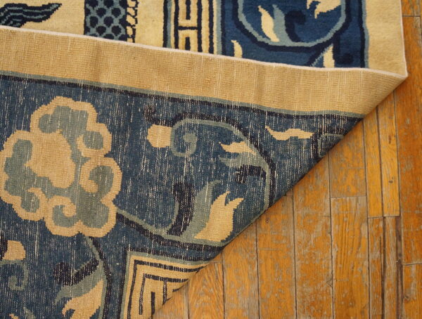 Blue and beige patterned rug folded over, displaying its backing on distressed wood planks.