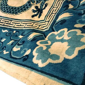 Close-up view of a blue and cream rug with dragon, Greek key, and stylized cloud patterns.