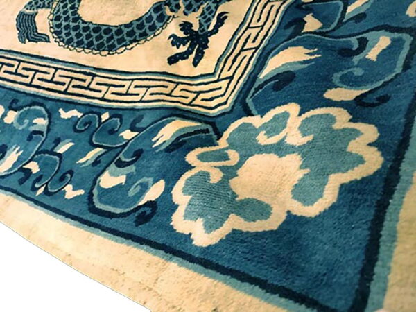 Close-up view of a blue and cream rug with dragon, greek key, and stylized cloud patterns.