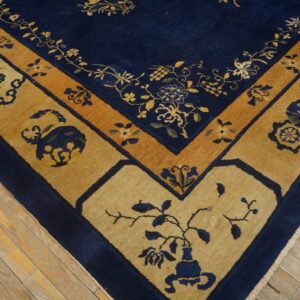 Blue rug with vibrant gold and tan stylized borders displaying floral and vase motifs on wood floor.