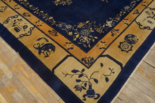 Blue antique rectangle 1920s wool hand knotted pile rug 4 Blue rug with vibrant gold and tan stylized borders displaying floral and vase motifs on wood floor.