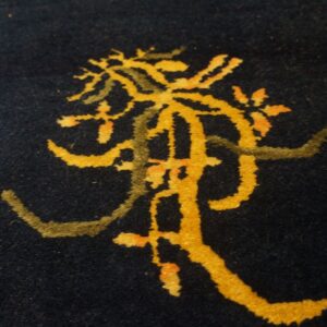 Close-up of a dark blue, low-pile rug featuring a stylized yellow and moss green abstract pattern.