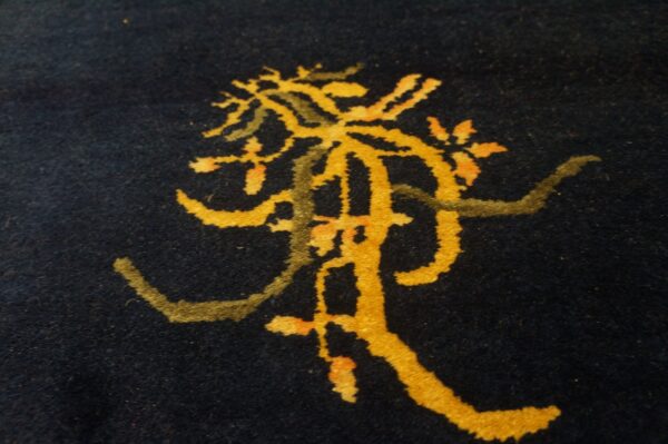 Blue antique rectangle 1920s wool hand knotted pile rug 5 Close-up of a dark blue, low-pile rug featuring a stylized yellow and moss green abstract pattern.