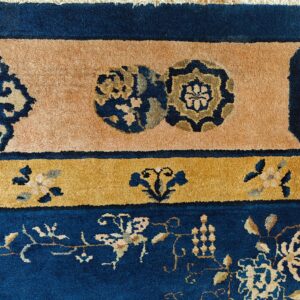 Detail of a plush rug in navy blue, gold, and peach, featuring layered floral and roundel borders.