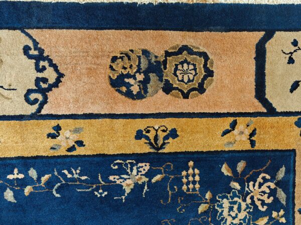 Blue antique rectangle 1920s wool hand knotted pile rug 7 Detail of a plush rug in navy blue, gold, and peach, featuring layered floral and roundel borders.