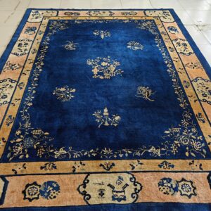Deep blue rug with gold floral designs and a tan and salmon border, displayed on white tile.