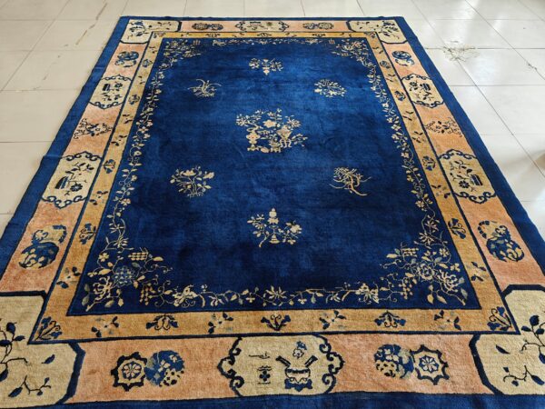Blue antique rectangle 1920s wool hand knotted pile rug 2 Deep blue rug with gold floral designs and a tan and salmon border, displayed on white tile.