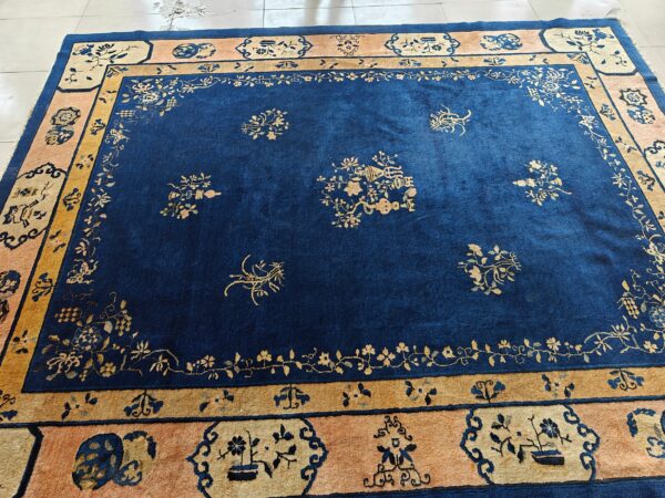 Blue antique rectangle 1920s wool hand knotted pile rug 3 Royal blue rug with gold floral motifs and peach and gold borders on light tile floor.