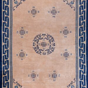 Tan and blue rug featuring a bold Greek key border and geometric central motifs on plank wood floor.
