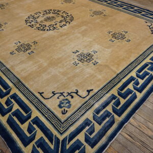 Low-pile tan rug with faded navy blue geometric patterns resting on distressed wood floors.