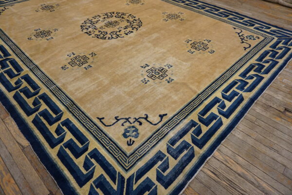 Low-pile tan rug with faded navy blue geometric patterns resting on distressed wood floors.