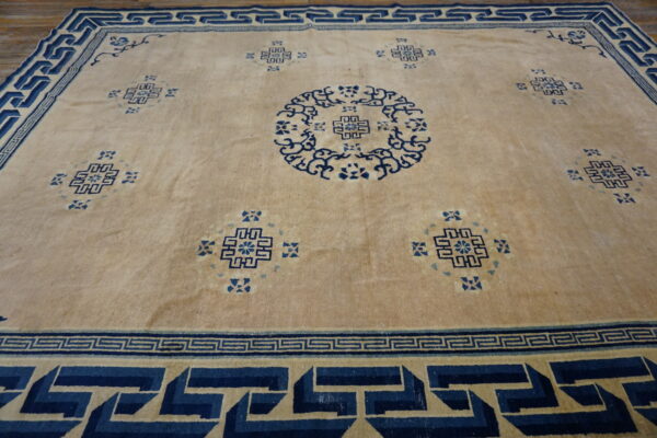 Low-pile rug in beige and dark blue displays large geometric medallions and complex stepped borders.