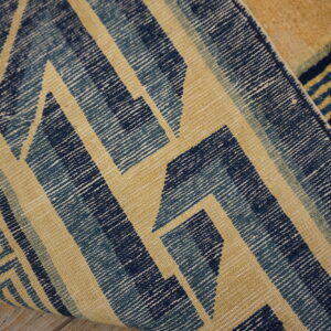 Blue and tan geometric rug detail curling, showing both flat-woven and high-pile textures on wood floor.
