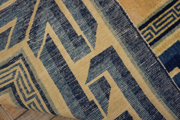 Blue and tan geometric rug detail curling, showing both flat-woven and high-pile textures on wood floor.