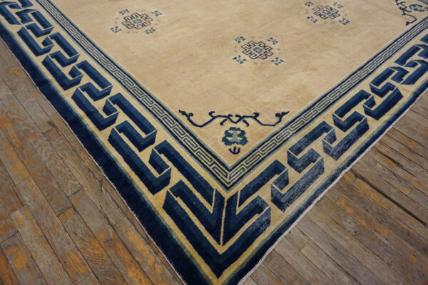 Beige rug with scattered blue patterns and a wide, complex navy optical border on rustic wood plank flooring.