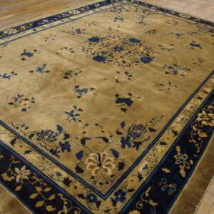 Muted olive green rug with deep blue and beige floral patterns displayed on light wooden plank flooring.