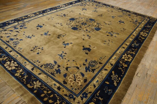 Muted olive green rug with deep blue and beige floral patterns displayed on light wooden plank flooring.