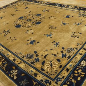 Gold and navy rug with a central floral medallion and multi-layered border on light wood flooring.