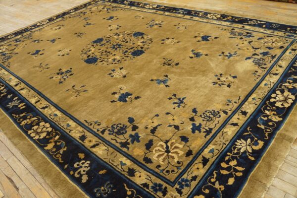 Gold and navy rug with a central floral medallion and multi-layered border on light wood flooring.