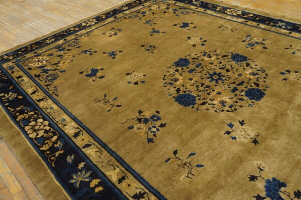 Mustard-gold rug with blue and beige floral patterns and wide navy borders rests on light wood flooring.