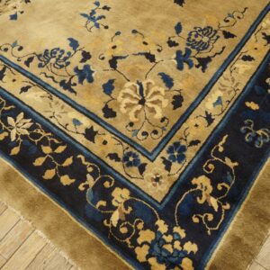Tan floral rug featuring a dark navy border with gold and blue accents on wood plank flooring.