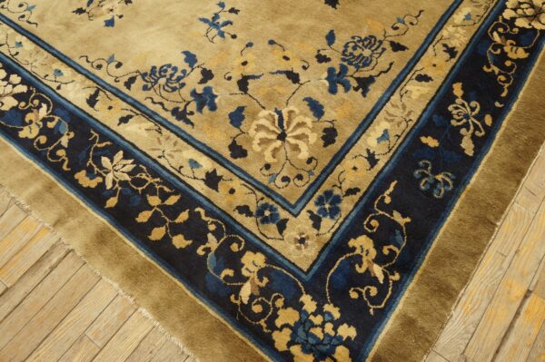 Tan floral rug featuring a dark navy border with gold and blue accents on wood plank flooring.