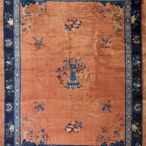 High-pile rectangular rug featuring a dusty orange field and elaborate navy blue borders with floral designs.