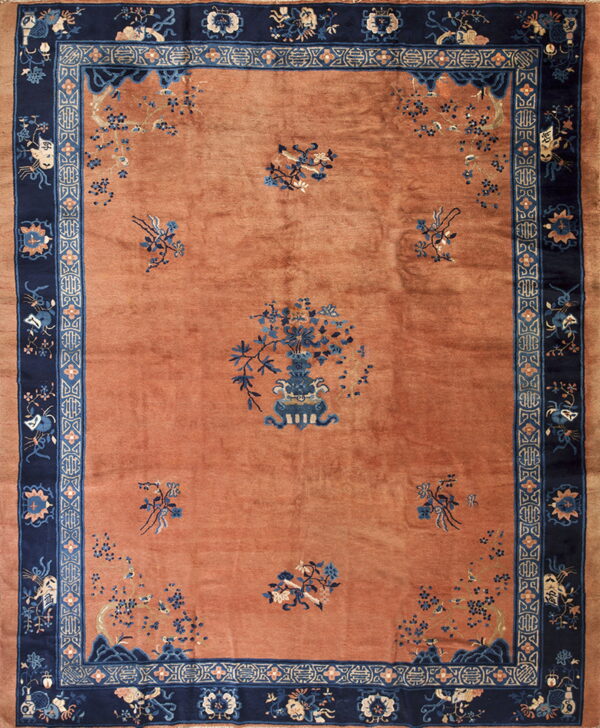 High-pile rectangular rug featuring a dusty orange field and elaborate navy blue borders with floral designs.