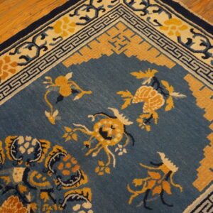 Blue field rug with gold botanical patterns and a geometric border rests on polished wood floors.