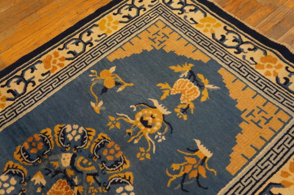 Blue field rug with gold botanical patterns and a geometric border rests on polished wood floors.