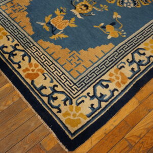 A corner of a blue and yellow patterned rug rests on distressed wood plank flooring.
