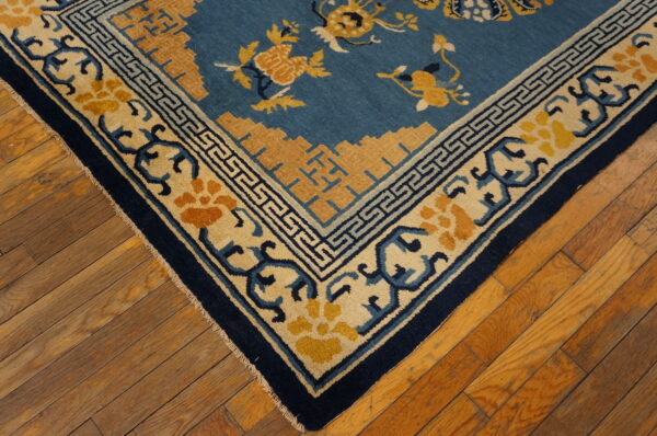A corner of a blue and yellow patterned rug rests on distressed wood plank flooring.