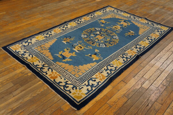Teal and gold floral patterned rug with dark blue borders on distressed wood floors.
