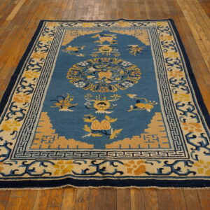Medium blue rug with yellow and cream floral patterns and a navy border, lying on wood plank flooring.