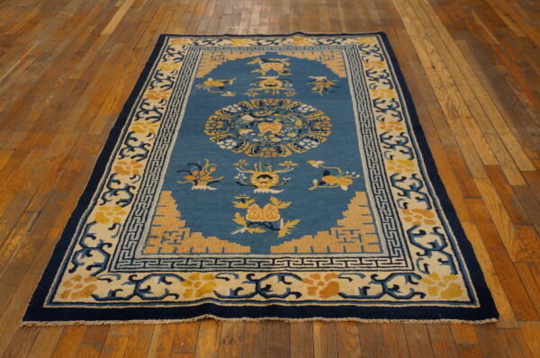 Medium blue rug with yellow and cream floral patterns and a navy border, lying on wood plank flooring.