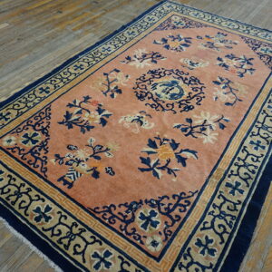 Peach-colored rug with blue and tan floral patterns and geometric borders sits on rustic wide plank wood floors.