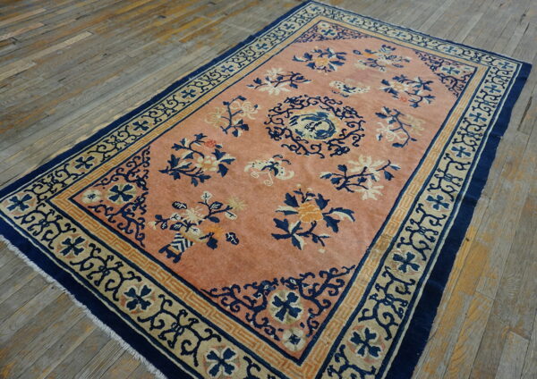 Peach-colored rug with blue and tan floral patterns and geometric borders sits on rustic wide plank wood floors.