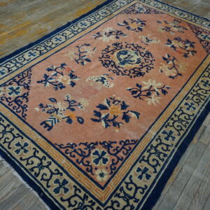 Coral rug with navy and beige floral designs and borders rests on rustic wood planks.