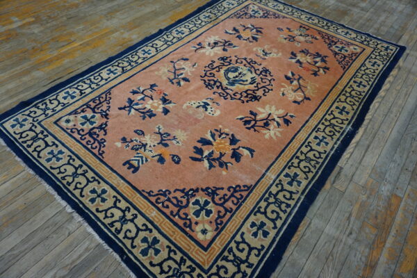 Coral rug with navy and beige floral designs and borders rests on rustic wood planks.